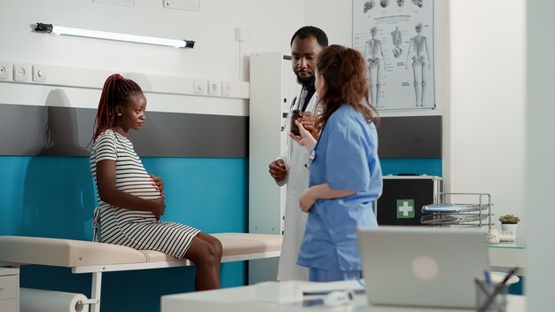 African american doctor giving prescription pills to pregnant patient at checkup visit. Male physician helping woman with pregnancy belly, showing bottle of medication treatment.