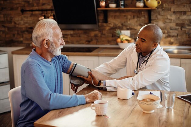 African American doctor measuring senior man's blood pressure at nursing home