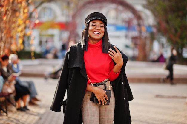 African american fashion girl in coat and newsboy cap with handbag posed at street