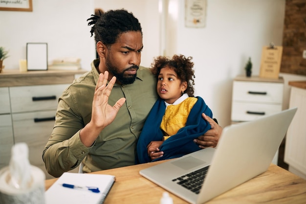 African American father and daughter having video call over laptop at home