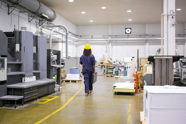 Free Photo african american female industrial employee in hardhat and overall walking on plant floor