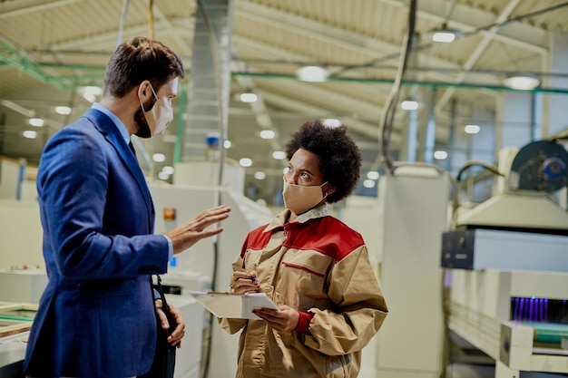 Free photo african american female worker and company manager wearing face masks while talking at woodworking factory