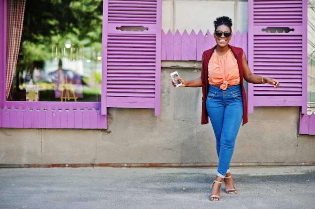 African american girl in sunglasses posed against purple windows with cell phone at hand