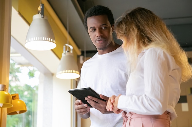 African American guy looking at blonde client and holding tablet