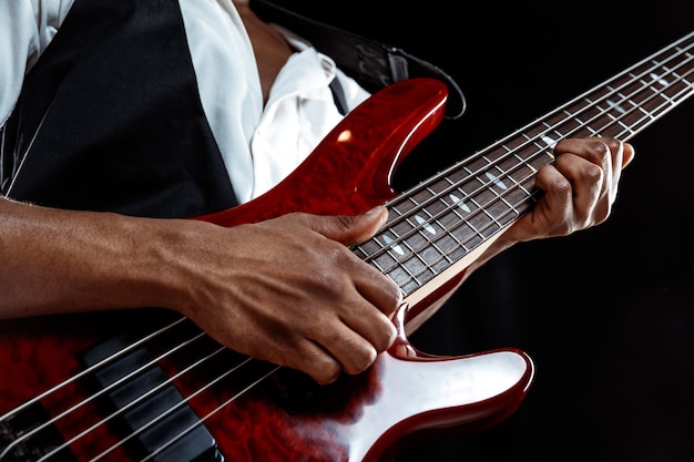 African American handsome jazz musician playing bass guitar in the studio on a black background. Music concept. Young joyful attractive guy improvising. Close-up retro portrait.