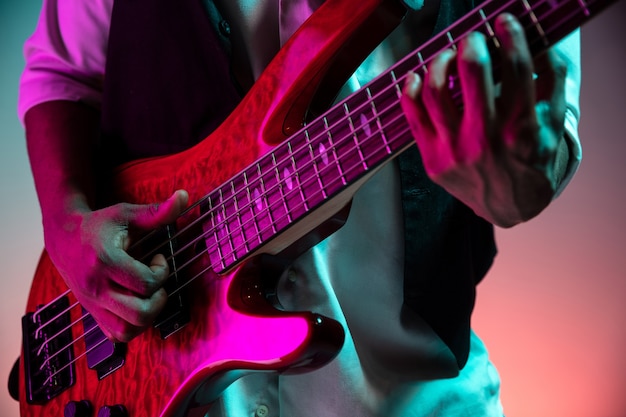 African American handsome jazz musician playing bass guitar in the studio on a neon background. Music concept. Young joyful attractive guy improvising. Close-up retro portrait.