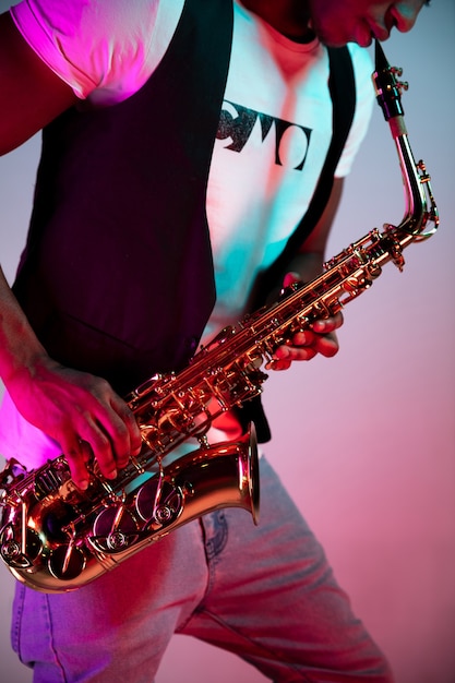 Free Photo african american handsome jazz musician playing the saxophone in the studio on a neon background. music concept. young joyful attractive guy improvising. close-up retro portrait.