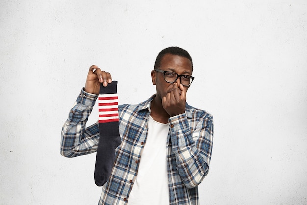 African American hipster pinching nose because of bad smell of dirty stinky sock in his hand