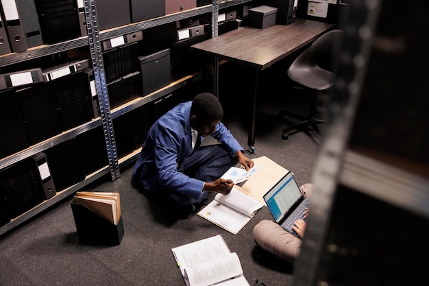 Free photo african american inspector searching for clues, analyzing crime scene evidence in arhive room. diverse private detectives working overtime at criminal investigation. law enforcement concept