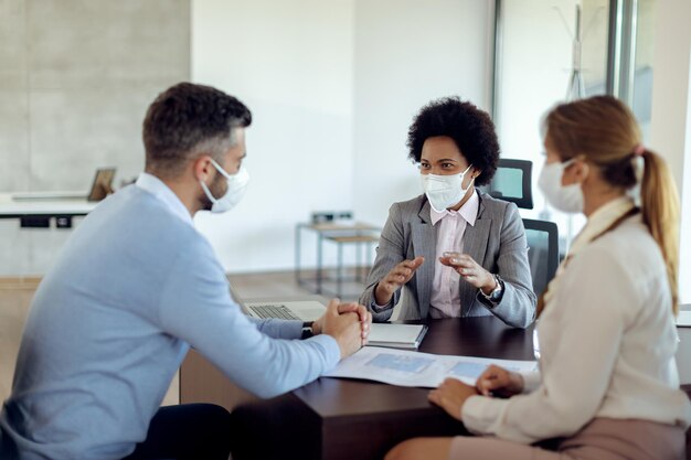 African American insurance agent with a face mask talking to her clients on a meeting in the office