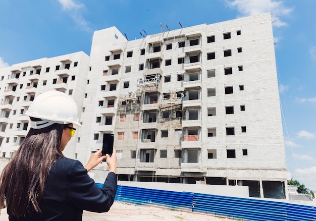 African American lady in safety helmet taking photo of building under construction