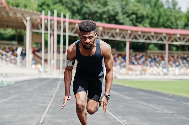 African american male athlete in sportswear racing alone down a running track at stadium