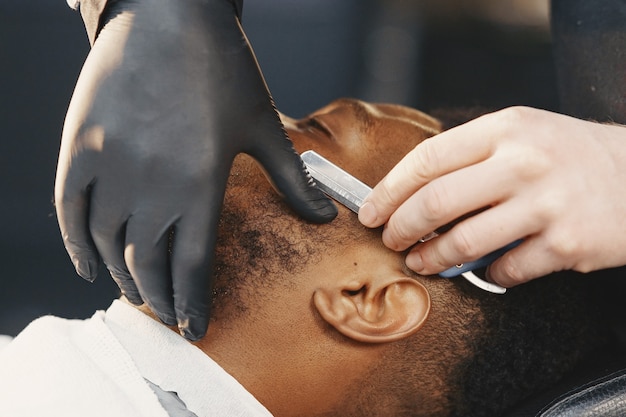 African American man. Guy sitting on a chair. Barber works with a beard.