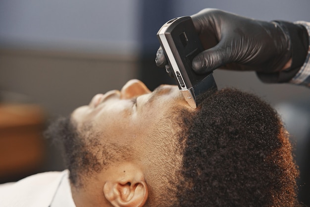 African American man. Guy sitting on a chair. Barber works with a beard.