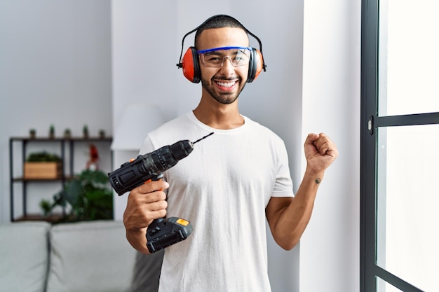 Free photo african american man holding screwdriver wearing ear protection at home screaming proud, celebrating victory and success very excited with raised arm