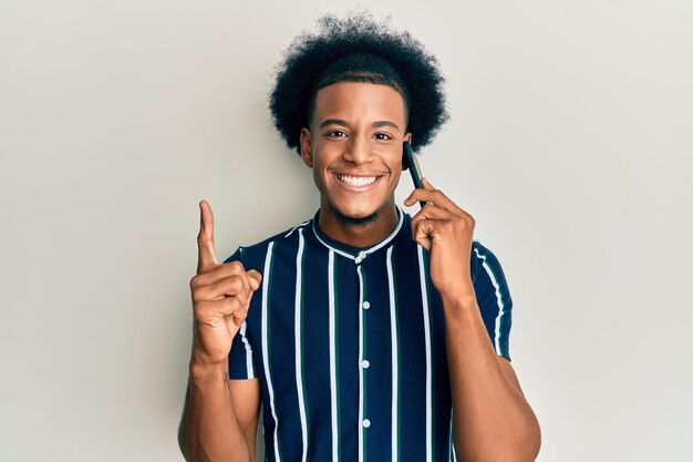 African american man with afro hair having conversation talking on the smartphone smiling with an idea or question pointing finger with happy face, number one