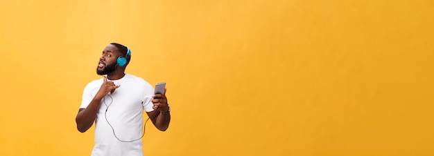 African american man with headphones listen and dance with music isolated on yellow background