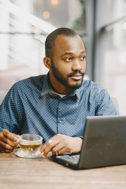 African-american man working behind a laptop. Man with beard sitting in a cafe and drink a tea.