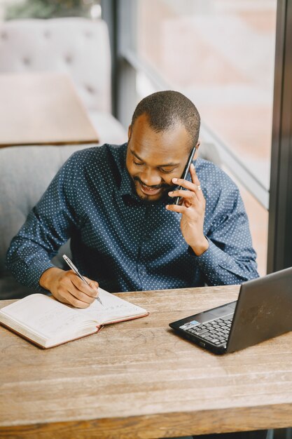 African-american man working behind a laptop and talking on the phone. Man with beard sitting in a cafe.