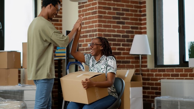 African american partners having fun with unpacked furniture in new household apartment. Enjoying relocation, moving in rented flat together and fooling around with decor. Handheld shot.