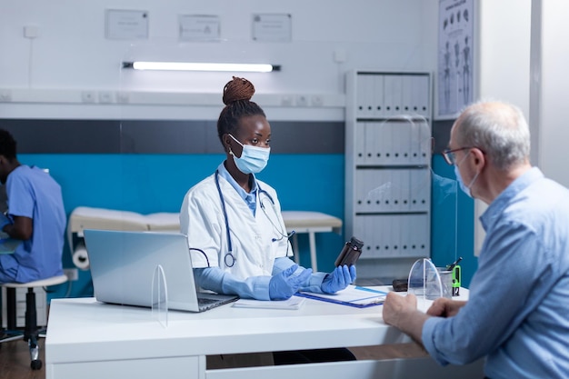 Free photo african american physician expert holding vial of covid medicine while talking to senior man about health risks. clinic specialist doctor conversating with retired man about virus pandemic outbreak