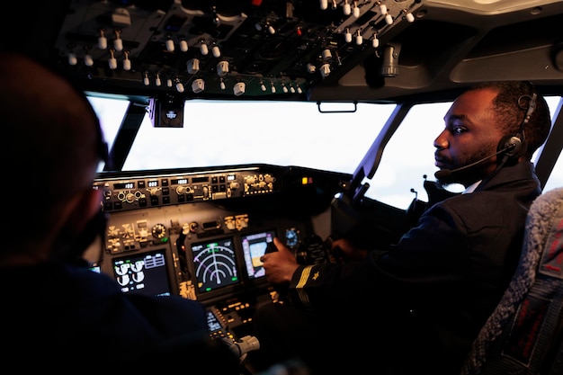 Free Photo african american pilot flying aircraft jet doing teamwork with captain, using dashboard command and navigation. team of airliners pushing control panel buttons and lever to takeoff and fly.