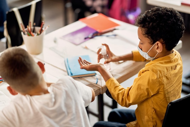 Free photo african american schoolboy using hands sanitizer in the classroom