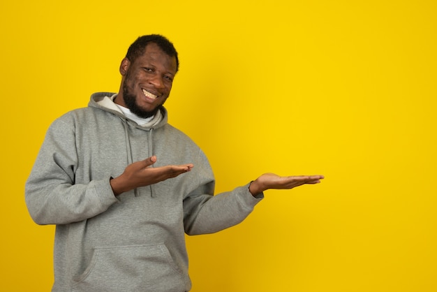 African-American smiling man who opened his hands , standing in front of the yellow wall. 