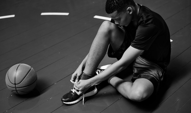 Free photo african american teenage boy tying his shoe laces on a basketball court