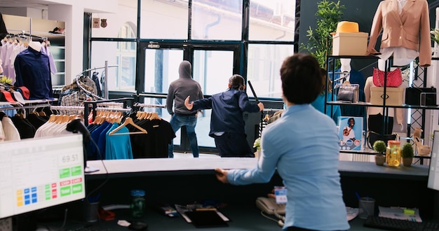 Free Photo african american thief stealing trendy clothes, running from shopping centre. asian bodyguard catches robber at store door, threatens him with the police in modern boutique. burglary concept