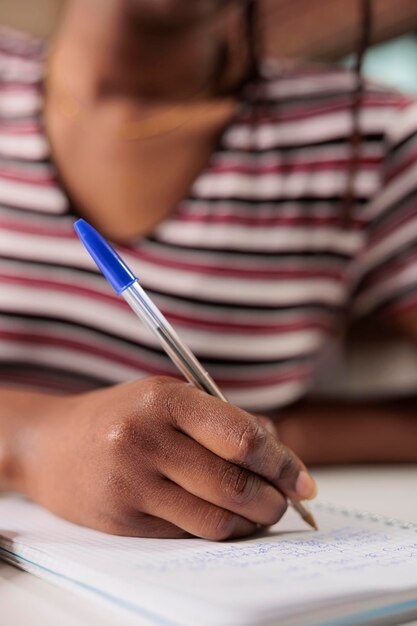 African american woman hand writing with pen in notepad at desk closeup. Student taking notes in planner close view, studying, preparing for exam, doing homework in notebook