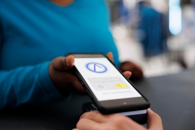 Free Photo african american woman paying for formal wear with mobile phone nfc on pos terminal, buying stylish clothes and accessories in modern boutique. shopper standing at retail store counter desk. close up