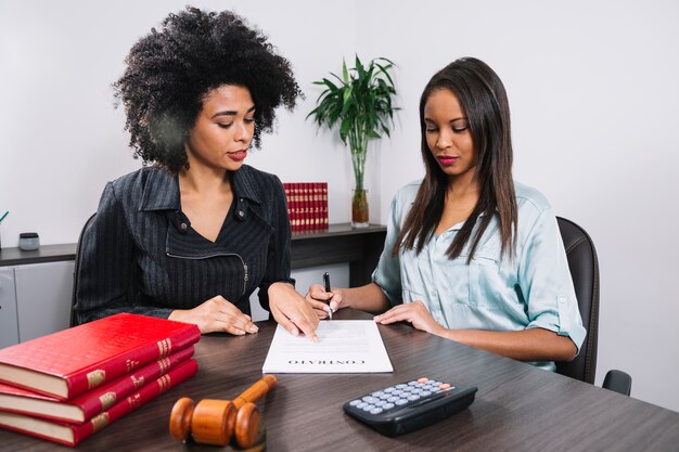 African American woman pointing at document near lady with pen at table