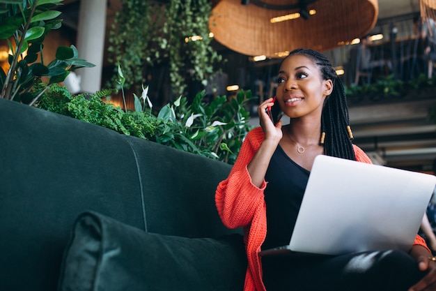 African american woman with phone and laptop in a cafe