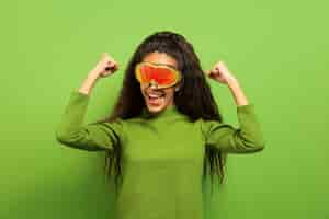 Free photo african-american young brunette woman's portrait in ski mask on green studio background. concept of human emotions, facial expression, sales, ad, winter sport and holidays. smiling, celebrating.