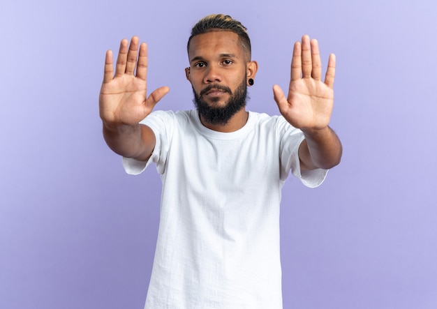 African american young man in white t-shirt lookingat camera with serious face making stop gesture