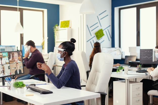 Free Photo african businesswoman wearing wireless headphones during online call with business people wearing face mask. new normal business office multiethnic team working respecting social distance during globa