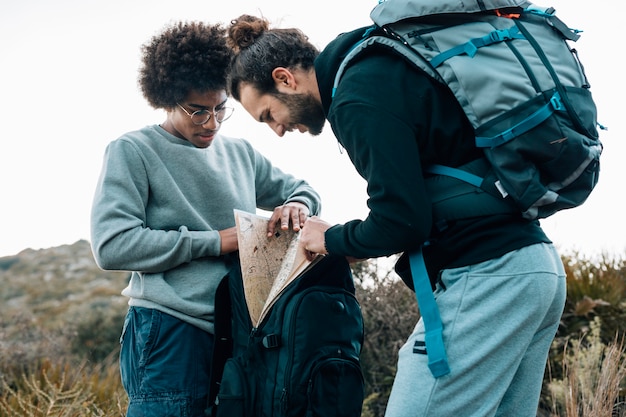 Free photo an african and caucasian young men looking for map in the backpack