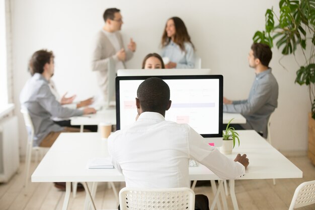 African employee working on computer in multiracial office, rear view