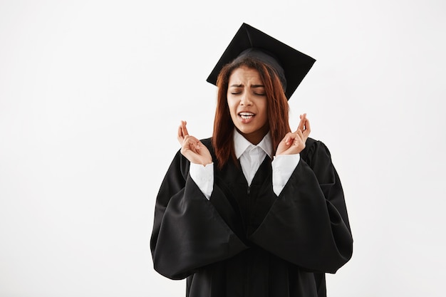 African female graduate in black mantle praying over white surface