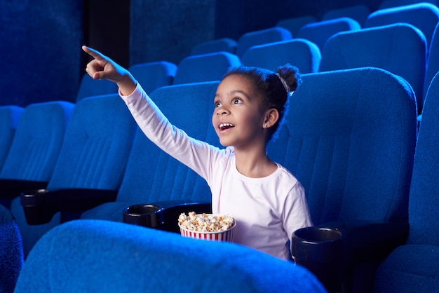 African girl poiniting with finger at screen in cinema.