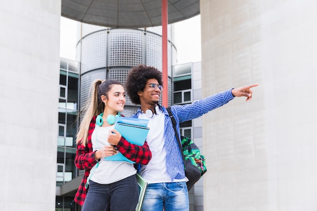 An african male students standing outside the university showing something to his female friend