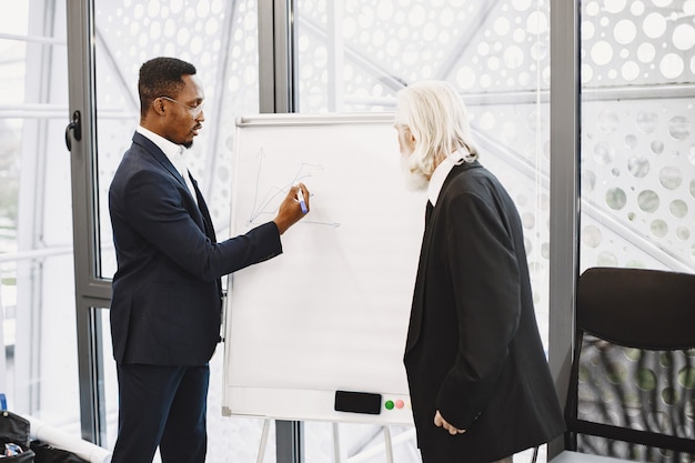 African man in a black suit. International partners. Young guy with senior man. Writing board.