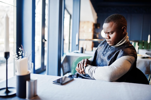 African man in black traditional clothes sitting at restaurant and looking at his watches