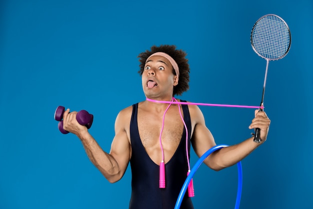 Free photo african man posing with dumbbells, hoop, skipping rope, racket