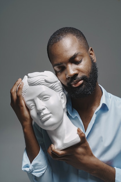 African man in a studio. White wall.  Man in a blue shirt.