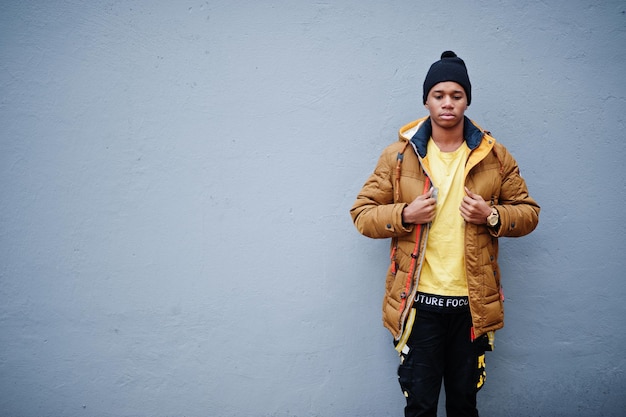 African man wear on jacket and black hat at cold weather posed outdoor against grey wall