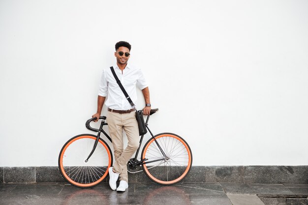 African man with bicycle standing on white wall