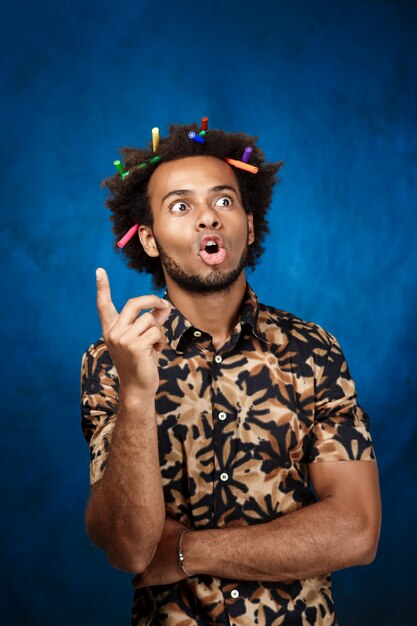 African man with markers in hair thinking over blue wall.