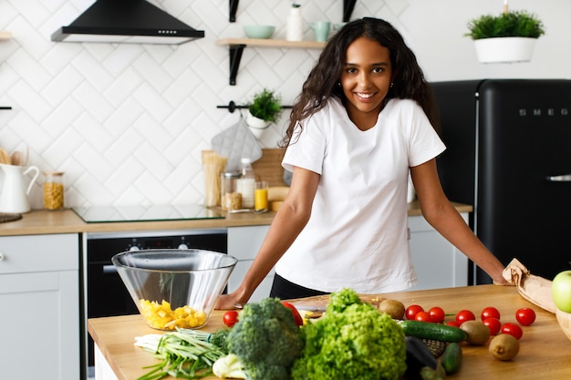 African woman stands before a kitchen desk with a different vegetables and fruits